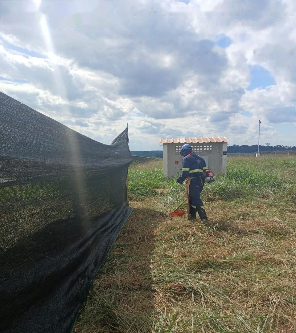 Operador roçando próximo à cabine com tela de proteção ao lado