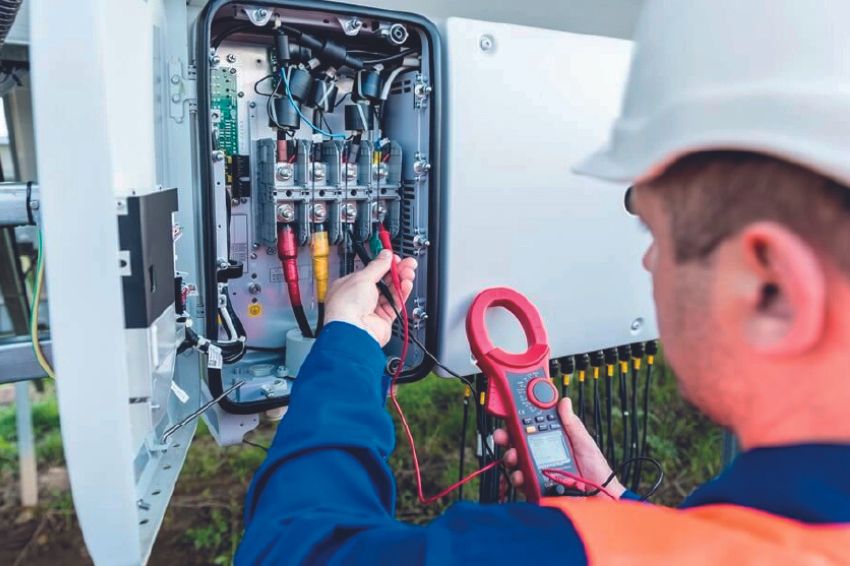 Técnico com capacete medindo corrente com alicate amperímetro em quadro de string box